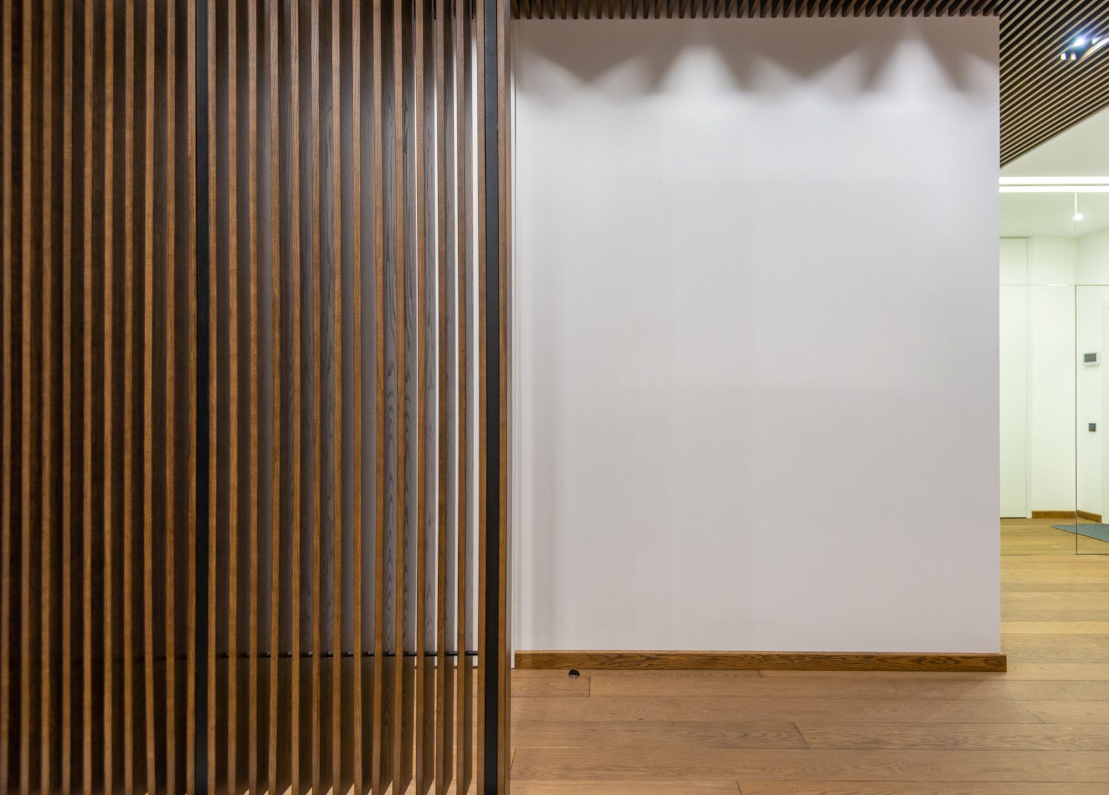 A slatted timber partition beside a white wall
