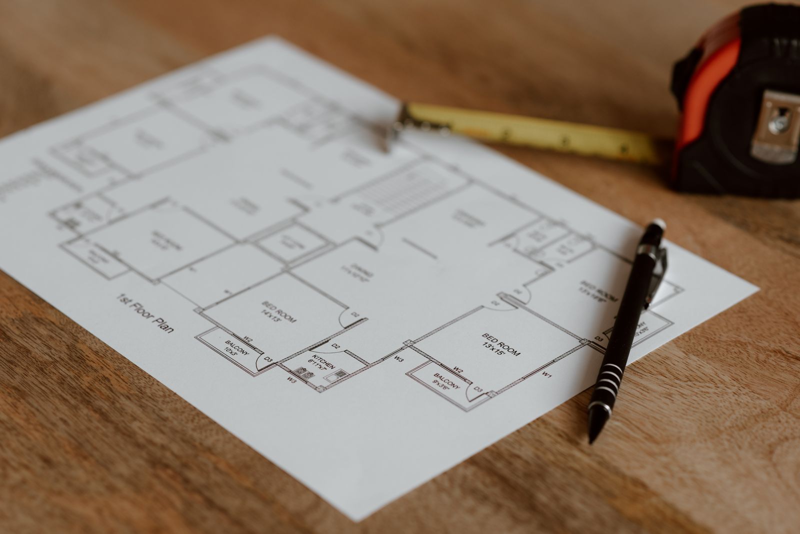 A floor plan on a timber desk with a tape measure and pen
