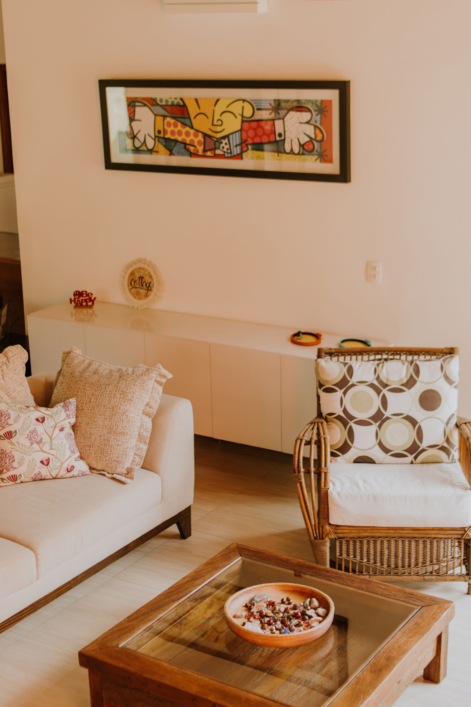 A warm living room with a white sofa, cane chair and framed art